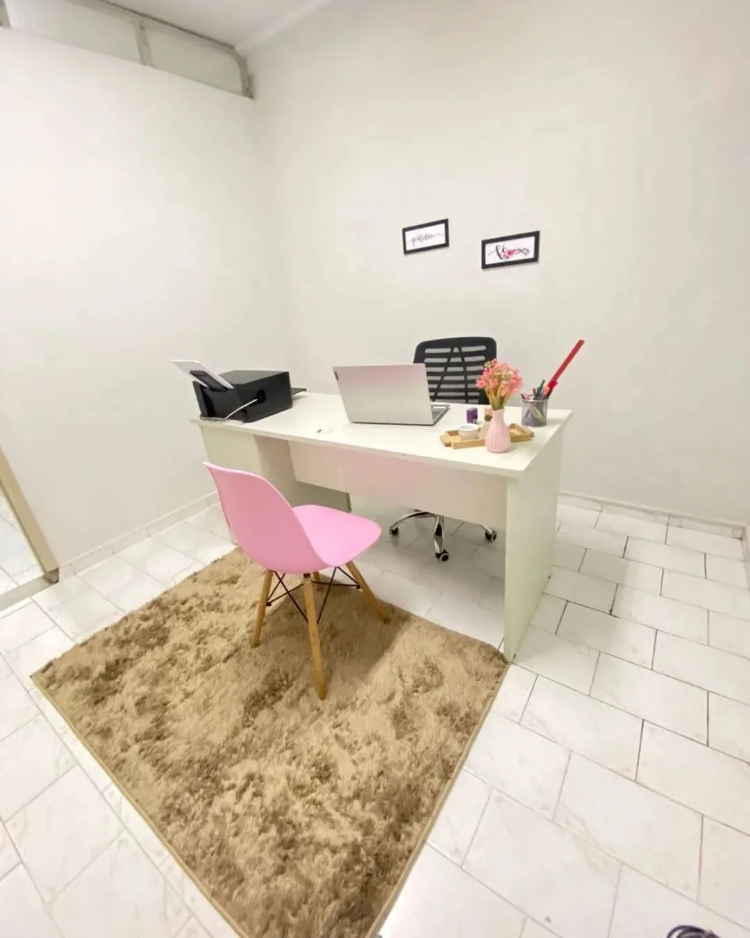 Sala de atendimento clara, com mesa branca, cadeira rosa e tapete