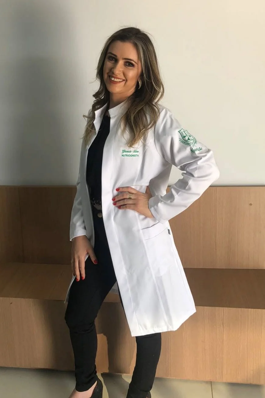 Gisleide Silva sorrindo, de jaleco branco bordado com o nome dela e a palavra nutricionista